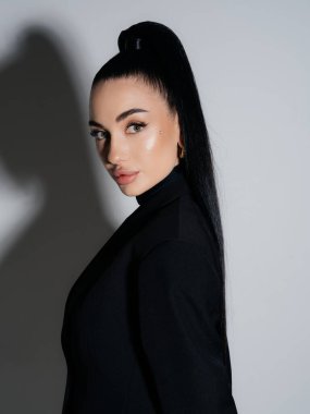 Yakın plan, zarif genç kadın portresi. Siyah ceket, yüksek atkuyruklu kamera. Profesyonel yönetici kadın model stüdyo çekimi. Tarz gücü güzellik kavramı.