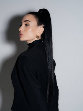 Sivri kenarlı, zarif, genç bir kadın portresi. Siyah spor ceket, uzun at kuyruğu. Profesyonel kendine güvenen kadın model stüdyo çekimi. Güzellik stili güç minimalizmi.