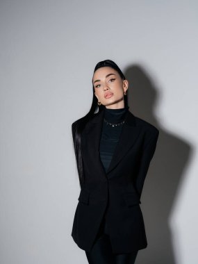 Siyah ceketli ve balıkçı yakalı zarif genç bir kadın elleri arkada duruyor. Kendine güvenen ciddi kadın yönetici profesyonel model stüdyo çekimi. Güç stili moda güzellik konsepti.