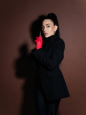 Zarif genç bayan kozmetolog doktor elinde şırınga tutan siyah ceketli kırmızı eldivenler. Estetik tıp yaşlanma karşıtı güzellik tedavi konsepti. Yan görünüm.