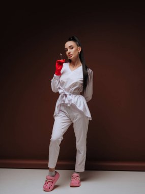 Zarif genç bayan doktor ya da hemşire kozmetolojist beyaz üniformalı kırmızı eldivenler ellerinde şırınga tutuyorlar. Estetik tıp Yaşlanma Karşıtı Prosedür.