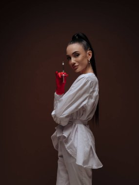 Gülümseyen genç bayan doktor ya da hemşire kozmetik uzmanı beyaz üniformalı kırmızı eldivenler şırınga manzaralı. Profesyonel estetik tıp prosedürü güven kavramı.