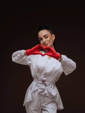 Beyaz üniformalı, kırmızı eldivenli, kalp hareketi yapan ve göz kırpan genç bayan doktor ya da hemşire. Profesyonel sağlık hizmeti, aşk ve bakım konsepti. Kliniğe hoş geldiniz..