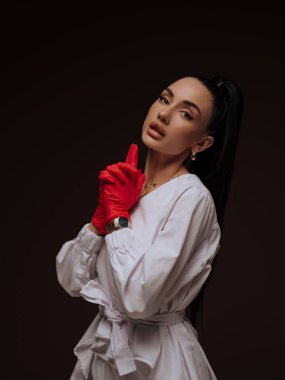 Kendine güvenen genç bayan doktor ya da hemşire kozmetolojist beyaz üniformalı kırmızı eldivenler işaret ediyor. Profesyonel estetik tıp ilgi ve uzmanlık konsepti.