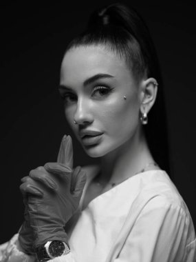 Genç doktor-kozmetik uzmanının ya da beyaz üniformalı hemşire ve eldivenli hemşirenin tek renkli portresi sessizlik jesti ile parmağını dudaklarına getiriyor. Mesleki gizlilik, hasta gizliliği sağlık hizmetleri.