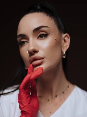 Yakın plan portre genç bayan doktor ya da hemşire kozmetolog beyaz üniformalı kırmızı eldiven yüzünü çeviriyor. Profesyonel estetik tıp, sağlık hizmeti kavramı.