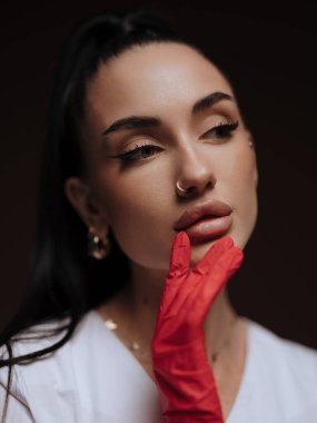 Yakın plan portre genç bayan doktor ya da hemşire kozmetolog beyaz üniformalı kırmızı eldiven yüzünü çeviriyor. Profesyonel estetik tıp, sağlık hizmeti kavramı.