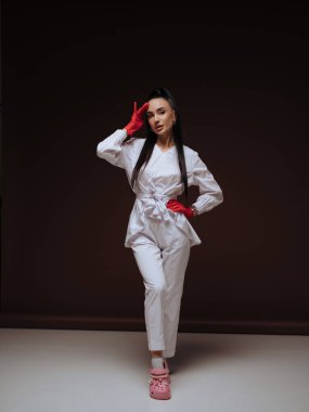 Kendine güvenen genç bayan doktor ya da beyaz üniformalı hemşire kozmetik uzmanı ve koyu arkaplanda duran kırmızı eldivenler. Profesyonel estetik tıp ve sağlık hizmeti kavramı.