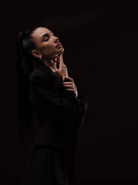 Elegant sensual young woman in black blazer posing with hand on neck and eyes closed. Fashion, beauty, relaxation, and skin care concept.