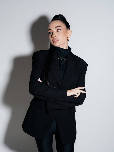 Elegant young woman wearing black blazer turtleneck posing with crossed arms. Confident serious female executive portrait studio shot. Power style fashion beauty concept.