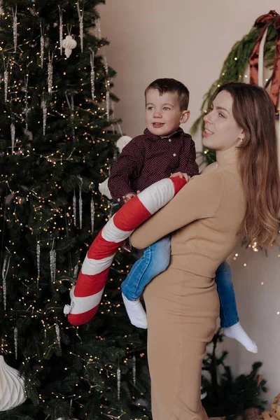 Küçük oğlunu kollarında tutan gülümseyen bir anne. Çocuğun elinde büyük, pelüş çizgili şeker kamışı var. Noel ağacının yanında süslerle, mücevherlerle ve ışıklarla süslenmiş bir odada duruyorlar..