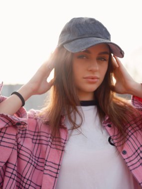 Uzun saçlı, şık giyimli ve şapkalı çekici bir kadın manken. Gün batımında büyük beden fanila gömlekli bir kıza yakın durun. Şehir modası ve gençlik yaşam tarzı konsepti.