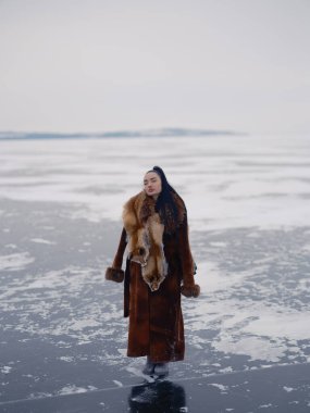Donmuş deniz buzunun üzerinde gözleri kapalı duran huzurlu genç bir kadın. Tilki postlarıyla süslenmiş uzun kahverengi kürk manto giyiyor. Sakin ve sakin bir atmosferi olan kışın ıssız kuzey manzarası.