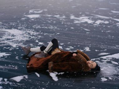 Lüks kışlık kürklü genç bir kadın ve donmuş su yüzeyinde uzanan bacak ısıtıcıları. Kontrastlı arka planda beyaz kar lekeleri olan koyu renk buz. Kuzey Kutbu 'nda poz veren modaya uygun bir kadın modeli..
