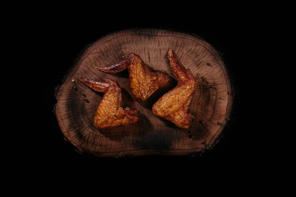 Τρία καπνιστά αρωματικά ζουμερά φτερά κοτόπουλου σε μια ξύλινη σανίδα. Άνω όψη. — Φωτογραφία Αρχείου