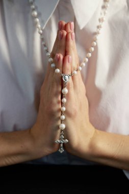 A young woman, in a white shirt folding a lodon to each other prays to God holding rosary.  clipart