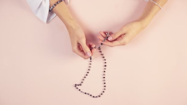 Ein junges Mädchen mit schönen Händen hält einen Rosenkranz in der Hand und betet. Angenehme und zarte Farben. — Stockvideo