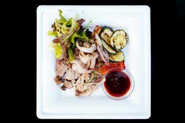 Beyaz tabakta domates soslu yeşil et salatası ve sebze.