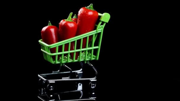 Winkelconcept. mini rode peper in een winkelwagen draaiend op een donkere achtergrond. — Stockvideo