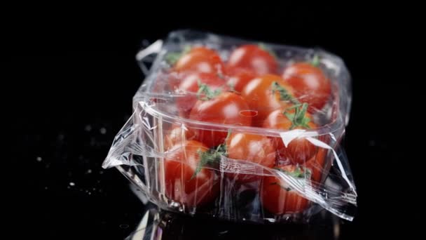 Tomates rojos frescos de cereza en una caja de plástico envuelta en un paño de aceite girando transparentemente sobre un fondo negro — Vídeo de stock