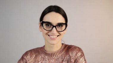Gri arka planda gülümseyen genç kadın. Stüdyoda gülümseyen mutlu kızın portresi. Moda mankeni gülüşünü kapat. Gözlüklü mutlu kadın kameraya bakıyor.