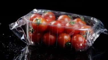 Plastik bir kutuya sarılı kırmızı kiraz domatesleri siyah bir arkaplanda dönüşüyor.