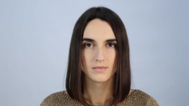 Duygusuz, genç esmer kız kameraya yakından bakıyor.