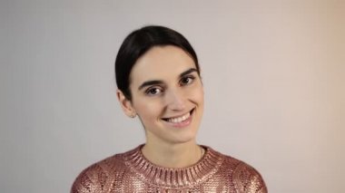 Stüdyoda mor bir süveter giyen güzel bir kız beyaz bir arka planda gülümsüyor ve çok mutlu.