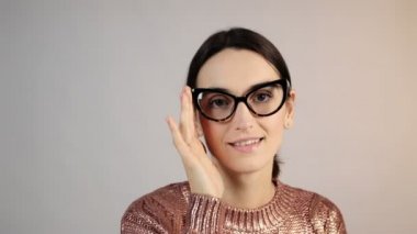 Gri arka planda gülümseyen genç kadın. Stüdyoda gülümseyen mutlu kızın portresi. Moda mankeni gülüşünü kapat. Gözlüklü mutlu kadın kameraya bakıyor.