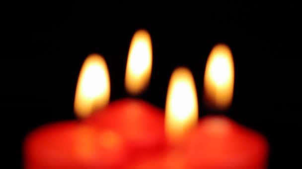 In sfocatura, quattro candele rosse stanno bruciando lentamente ruotando su uno sfondo nero — Video Stock