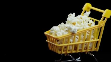 Siyah arkaplan boşluğunda patlamış mısırla dolu sarı alışveriş sepeti.