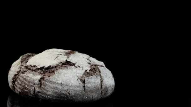黒い背景に小麦粉を振りかける新鮮な黒パンの回転. — ストック動画