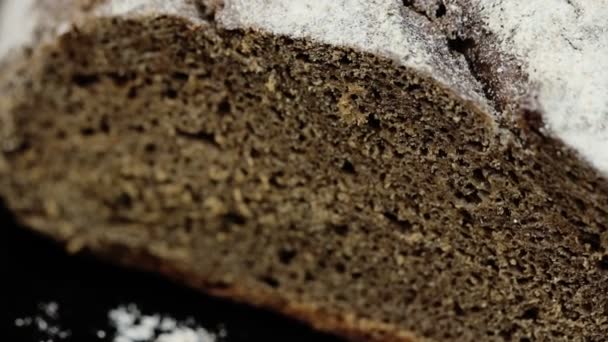 Pane nero fresco ruotante cosparso di farina su fondo scuro. Da vicino. — Video Stock