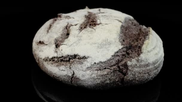 黒い背景に小麦粉を振りかける新鮮な黒パンの回転. — ストック動画