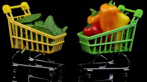 Twee boodschappenmanden gevuld met spinazie en paprika 's, gezond eten, groenten. Draaien op een zwarte achtergrond. — Stockvideo