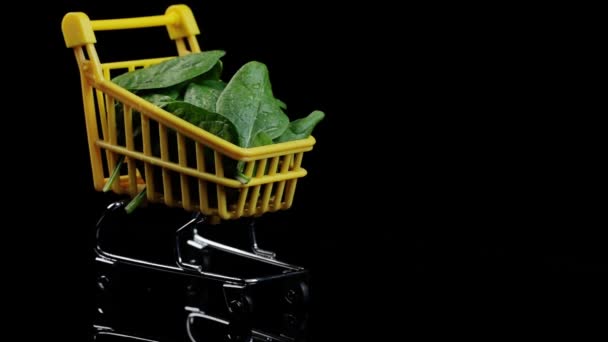 Filled with fresh slices of mini spinach for shopping rotating on a black background. The concept of shopping and healthy eating. — Stock Video