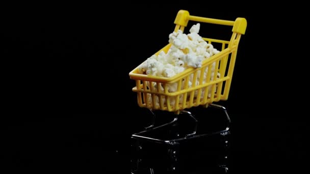 Sárga bevásárlókosár tele popcorn örvények egy fekete háttér szöveges — Stock videók