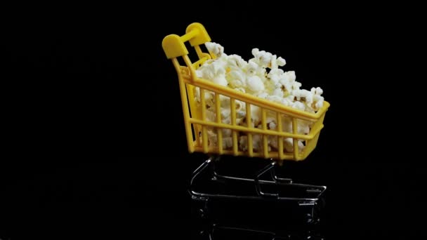Cesto de compras amarelo cheio de pipocas redemoinhos em um espaço de fundo preto para texto — Vídeo de Stock