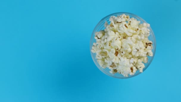 Popcorn in a plate on one edge of the frame, rotating on a blue background. Space for text. — Stock Video