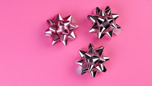 Három ezüst ajándék íj pörög a rózsaszín háttér — Stock videók