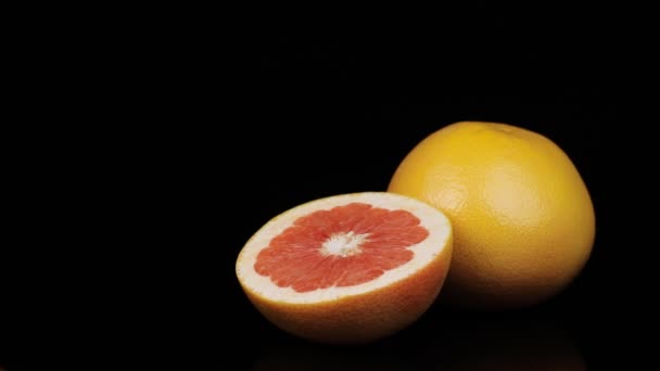 Frische Grapefruits, die sich im Kreis drehen, schwarzer Hintergrund und Platz für Text. Spiegelungen und Wasserklappen. — Stockvideo