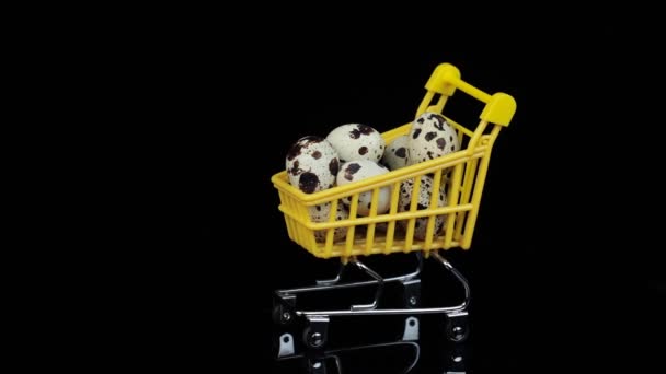Обертається. Перепелині яйця в жовтому кошику для покупок на чорному тлі . — стокове відео