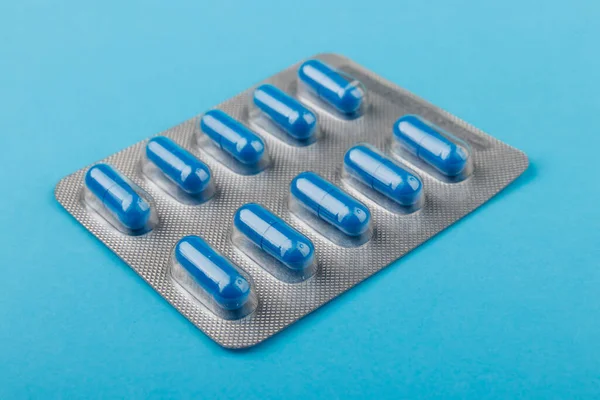 Tema da farmácia, pílulas azuis em cápsulas, fundo azul, medicina. — Fotografia de Stock