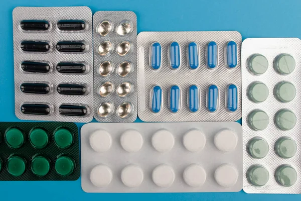 Heap of pills in blister packaging on blue desk. Concept of healthcare, drug addict or chemical weapon. Close-up. — Stock Photo, Image