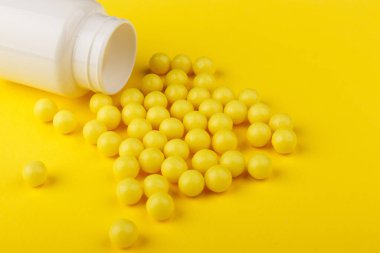 Sarı renkli C vitamini kapsülleri sarı arka planda beyaz bir kavanozdan dökülmüş. Sağlığına dikkat et. Vitamin ve mineraller. Boş alan