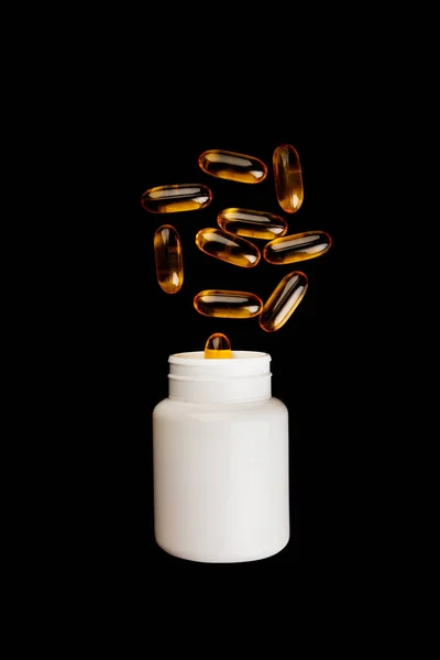 Healthy diet concept. Fish oil capsules with omega 3 and vitamin D in a plastic bottle on a black background. Stock Photo
