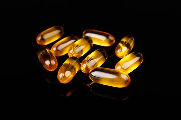 Capsules with fish oil on a black background. The use of vitamin D, omega-3. Health concept 스톡 사진