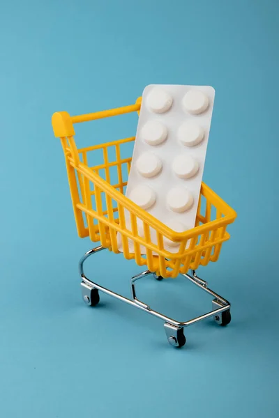 Shopping cart on a blue background with a medicine plate white pills inside Stock Photo