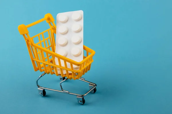 Shopping cart on a blue background with a medicine plate white pills inside Stock Picture