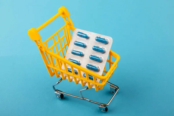 Shopping cart loaded with pills on blue background. The concept of medicine and the sale of drugs. Copy space. Stock Picture